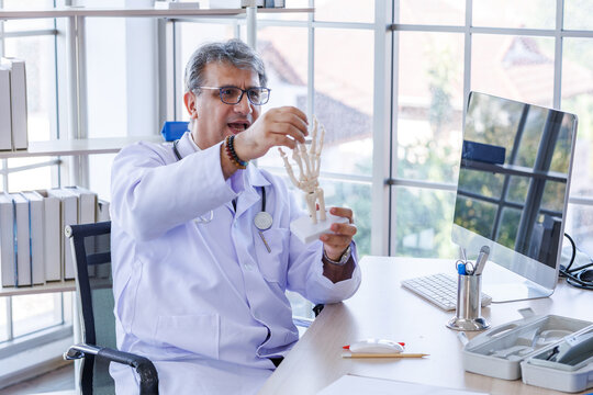 Doctor holding and pointing at foot skeleton anatomical model during patient consultation at the bones while explaining medical conditions or anatomy at his office desk a hospital clinic