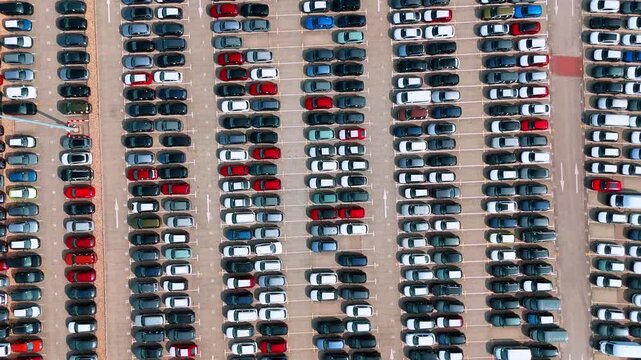Parked cars form parallel rows across a paved lot. An overhead view shows alternating dark and light vehicles with red and blue accents.