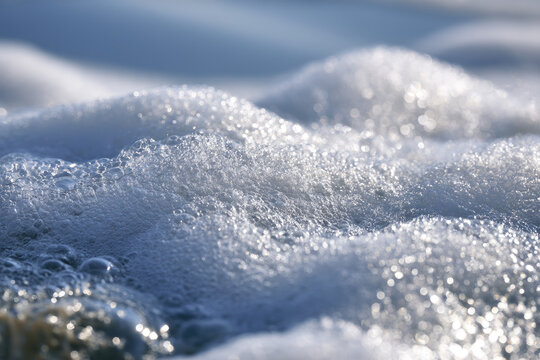 Snow foam texture with sparkling ice crystals, soft blue shadows, and bright winter sunlight creating calm abstract natural surface