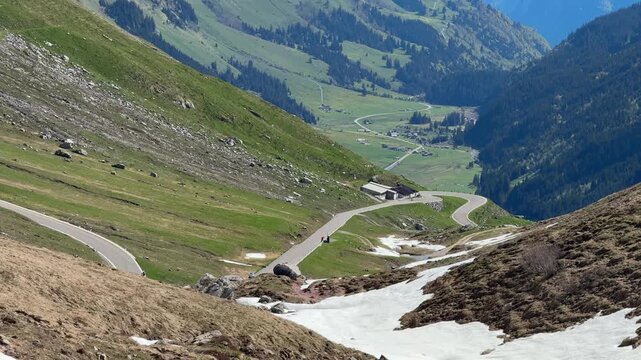 View down from Klausen Pass towards Linthal, Switzerland, during spring pass opening, with alpine road, green slopes and traces of snow in higher elevations.