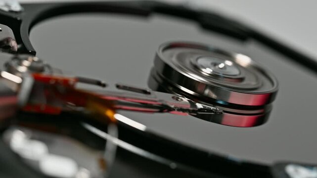 Extreme close up of data storage drive internal components showcasing a mirrored disk and metallic arm. Focus on precision engineering in modern data storage devices.