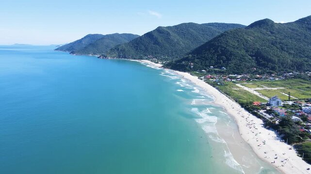 Drone aerial panoramic view of Praia dos Acores coastline looking towards Solidao beach and Saquinho cape in Florianopolis, Brazil, featuring turquoise ocean waters and green mountains
