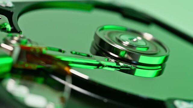 Extreme close up of internal components of a data storage drive under blue lighting. Focus on the reflective disk platter mechanism and intricate details of electronic components.