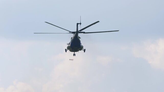 Civil transport helicopter flies overhead while aerobatic team of propeller planes passes in formation behind it at air show, hazy blue sky with clouds, telephoto shot