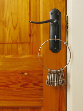 Wooden door with black handle and master key ring. Key ring holds many keys, hanging near lock. Image shows everyday home security detail. Useful for real estate, locksmith, or home decor themes