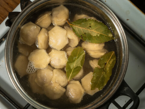 Dumplings in a pot of hot boiling water with bay leaf. Popular Russian dish. Cooking simple tasty food. Fine fast food meal with different flavour.