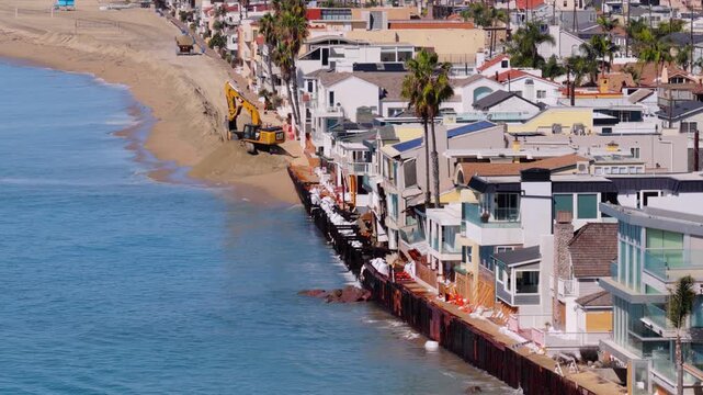 Long Beach, California, USA - October 15, 2026: Excavator and dump truck build a sand berm beside the broken seawall and damaged homes on the Peninsula after Tropical Storm Rachel.
