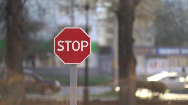 Red octagonal stop sign on metal pole in urban street with blurred cars and trees in daytime.