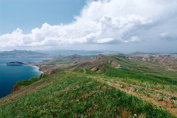 Expansive panoramic landscape of green rolling hills descending to blue ocean bay under dramatic clouds, evoking freedom and outdoor adventure ideal for travel, nature and environmental themes © Loginova