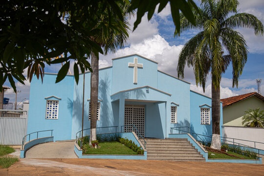 Par&oacute;quia Nossa Senhora da Guia com detalhe de galhos de &aacute;rvore na frente e c&eacute;u nublado ao fundo.