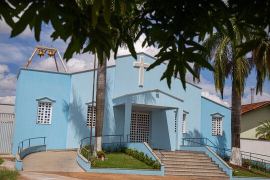 Par&oacute;quia Nossa Senhora da Guia com detalhe de galhos de &aacute;rvore na frente e c&eacute;u nublado ao fundo.