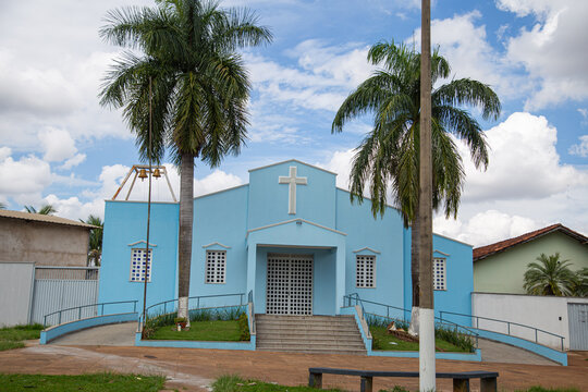 Par&oacute;quia Nossa Senhora da Guia com dois coqueiros na frente e c&eacute;u nublado ao fundo.