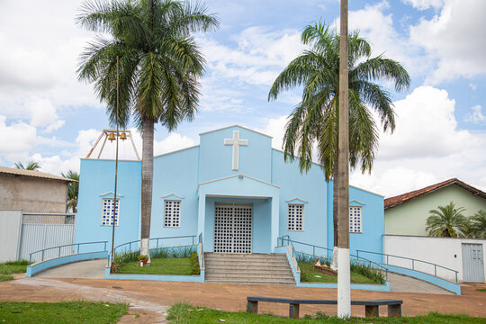 Par&oacute;quia Nossa Senhora da Guia com dois coqueiros na frente e c&eacute;u nublado ao fundo.