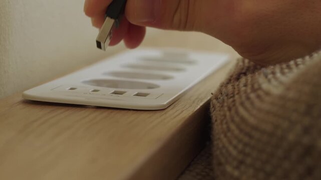 Person unplugging usb cable from wooden bedside socket