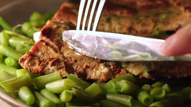 Cutting grilled salmon breast with green beans on plate
