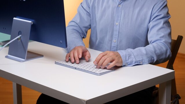 Office worker typing on a desktop keyboard at a white desk, using a computer workstation for business tasks, communication, data entry and everyday productivity in a modern indoor office