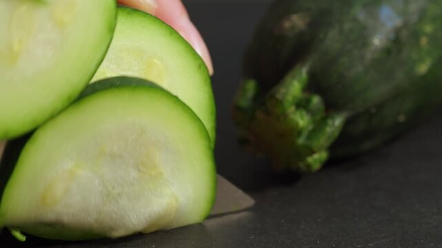 Slicing fresh green zucchini with knife on dark cutting board