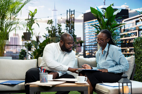 Business meeting, documents and colleagues frame two professionals reviewing papers together. Collaboration, project planning and decision making support teamwork in city terrace lounge.