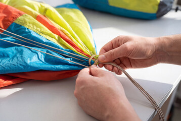 Obraz premium A rigger carefully secures the lines of a colorful parachute canopy with a rubber band during packing.
