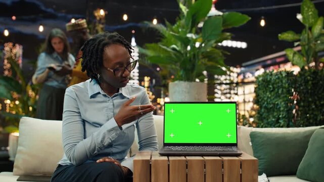 businesswoman speaks beside a rooftop green screen laptop, presenting a replaceable display for advertising, business branding or product mockups.