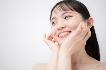 Fototapeta na wymiar 白背景で顎や頬に両手を添える10代～20代のような若い女性の美容やビューティーの見上げる笑顔　ニキビや思春期の肌の嬉しいハッピーなティーンのイメージ