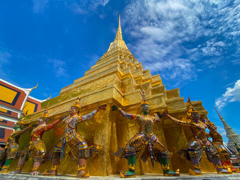 Majestic golden stupa supported by mythical demon and monkey statues against a blue sky at Wat Phra Kaew, Bangkok.