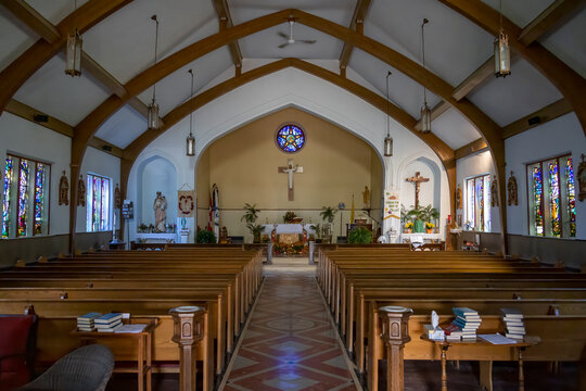 A serene view inside St. Bonaventure Church, Killarney, Ontario. Features wooden pews, stained glass windows, and a central altar with crucifix.
