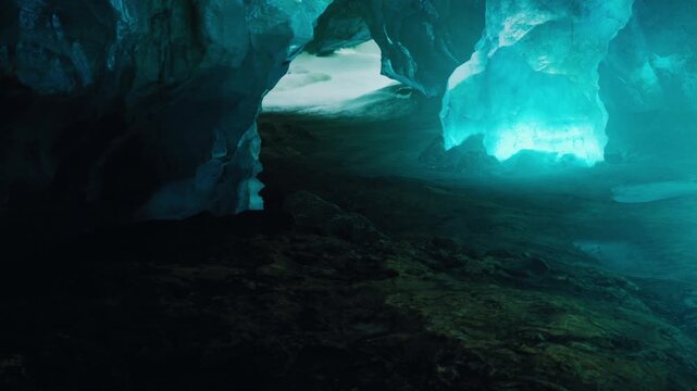 Sunlight illuminates the thick walls of translucent blue ice inside this cavern while snow covers the ground in the background during the bright hours of a cold winter day in Iceland