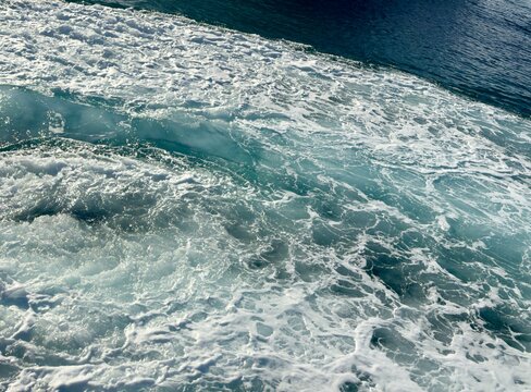 A high-contrast texture of dynamic white foam and churning turquoise ocean water created by a moving ship.