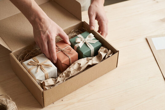 Hands arranging wrapped gifts in a cardboard parcel