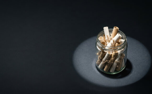 Glass jar filled with rolled wish notes and messages in a dramatic spotlight on a dark table surface