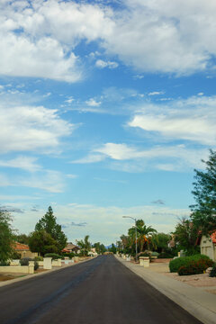 Suburban asphalt street in a quiet neighborhood under beautiful blue autumn sky with fluffy clouds in Phoenix, Arizona; copy space