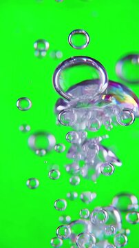 Slow motion macro shot of diverse water bubbles rising vertically against a bright green screen background