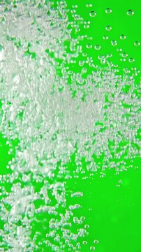 Tiny carbonated bubbles dispersing across a solid green screen backdrop with smooth fluid motion