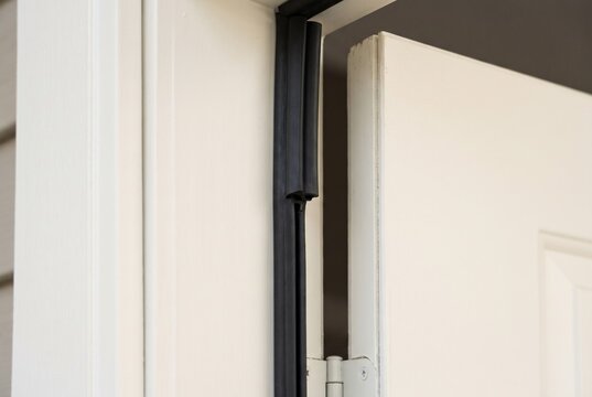 Close up of black rubber weather stripping seal installed on modern white door frame for energy efficiency and draft protection. 

