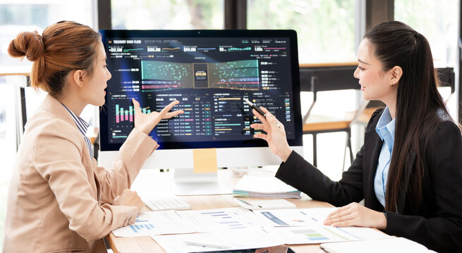 Two Asian Businesswomen Analyzing Financial Graphs on Computer Screen in Office