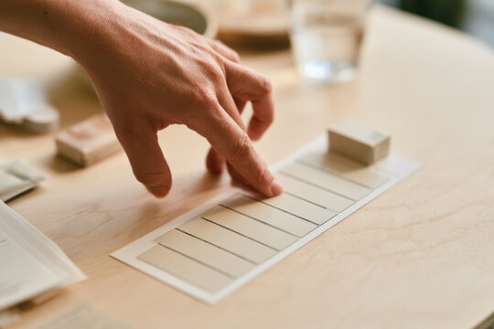 A close-up view of a hand selecting color shades from a swatch for design purposes on a minimalistic set up, showcasing creativity and attention to detail.