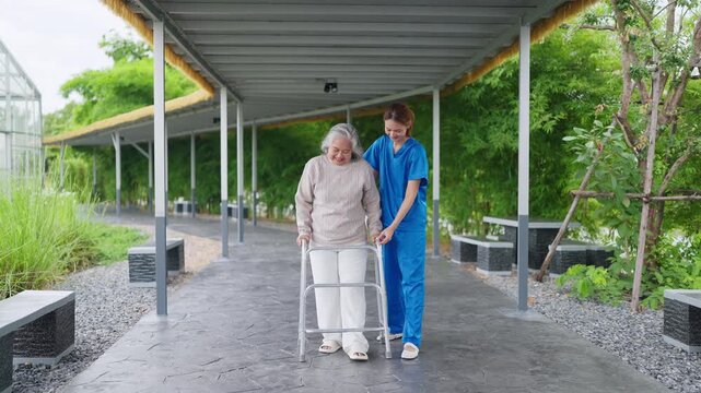 Senior woman uses walker with caregiver support. Caregiver smiles, offers gentle assistance. Covered walkway shelters them from sun and rain