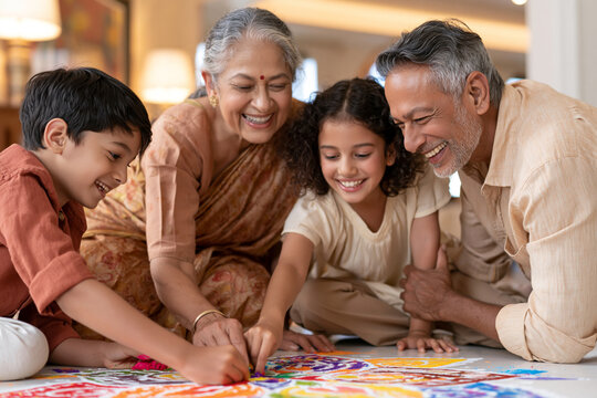 Grandparents and grandchildren laugh together. They sit on the floor, painting with colorful powder. The children smile as they work side by side. The elderly woman beams with joy