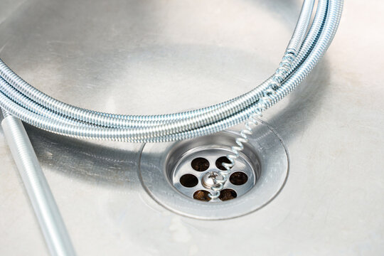 Plumbing maintenance and drain cleaning, metal plumbing snake tool inserted into a kitchen sink drain to remove a clog for home repair and renovation