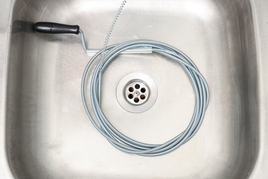 Plumbing maintenance and drain cleaning, metal snake tool coiled in a stainless steel kitchen sink for home repair and pipe blockage removal service