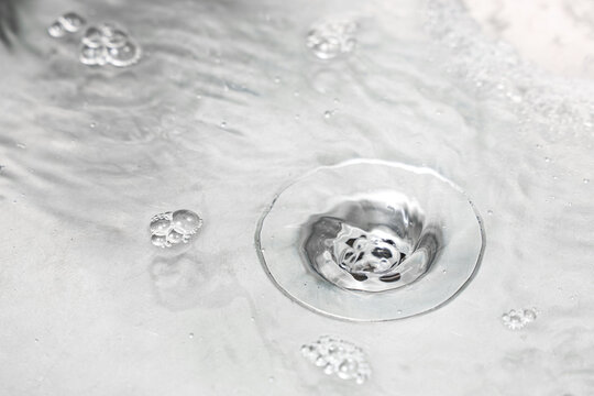Water conservation and sustainability, clear water swirling down a metal sink drain with soap bubbles and liquid vortex in a modern kitchen or bathroom