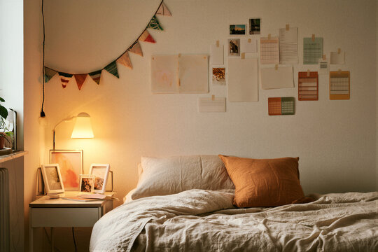 Cozy international student dorm room with tidy single bed, neutral cotton-linen bedding, warm yellow desk lamp, small flag pennants, photo frames and blank postcards, study abroad landing page mockup