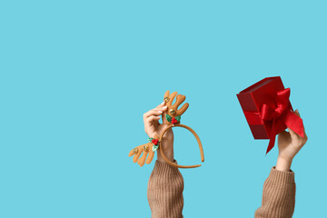 Female hands with Christmas reindeer horns headband and gift box on blue background © Pixel-Shot