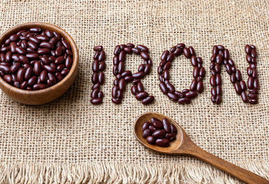 Fresh black kidney beans arranged creatively spelling iron on rustic burlap fabric with wooden bowl and spoon