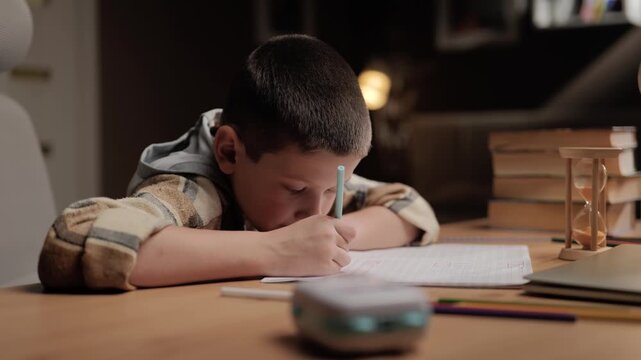 Tired little schoolboy doing homework at home sitting hunched over notebook. Fatigue posture studying academic stress concept