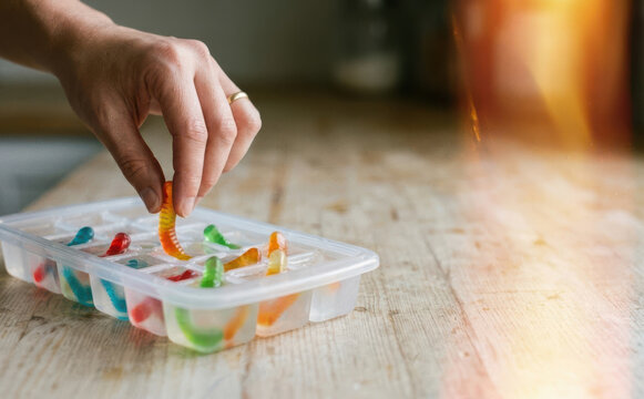 Woman preparing gummy worm ice cubes for a fun summer party drink preparation on a wooden kitchen table