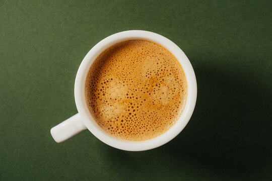 A cup of coffee with crema on a dark green background