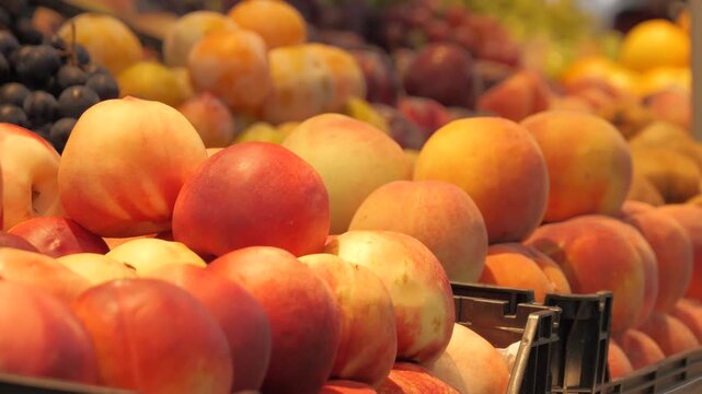 The camera pans across peaches stacked in black plastic crates at a market, with bunches of grapes visible behind them.