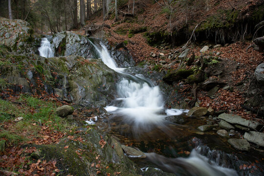 Small cascading waterfall flowing over rugged rocks in an autumnal forest landscape